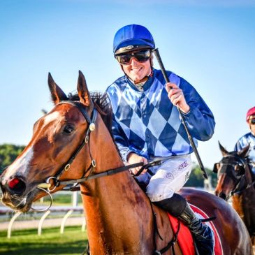 Jockey smiling on a horse at a racetrack.
