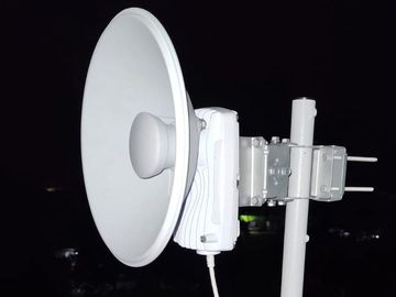 White satellite dish mounted on a pole at night.