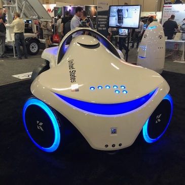 Futuristic autonomous vehicle with glowing blue wheels displayed at a tech expo.