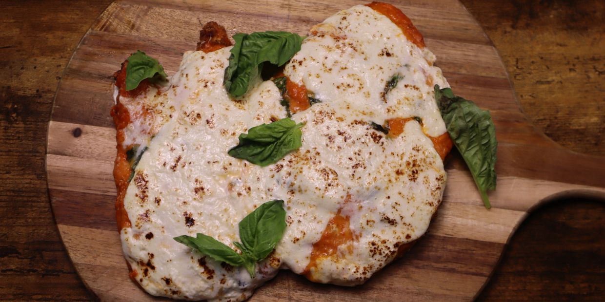 Three cheesy chicken parmesan pieces garnished with basil on a wooden board.