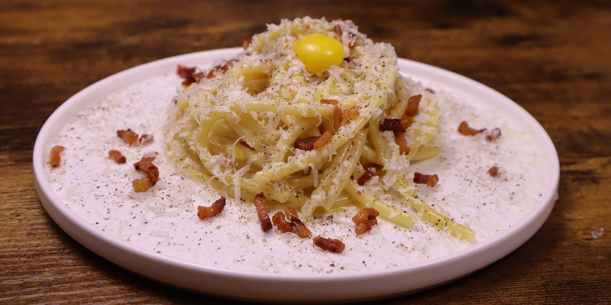 Plate of pasta carbonara with grated cheese, bacon bits, and egg yolk on top.