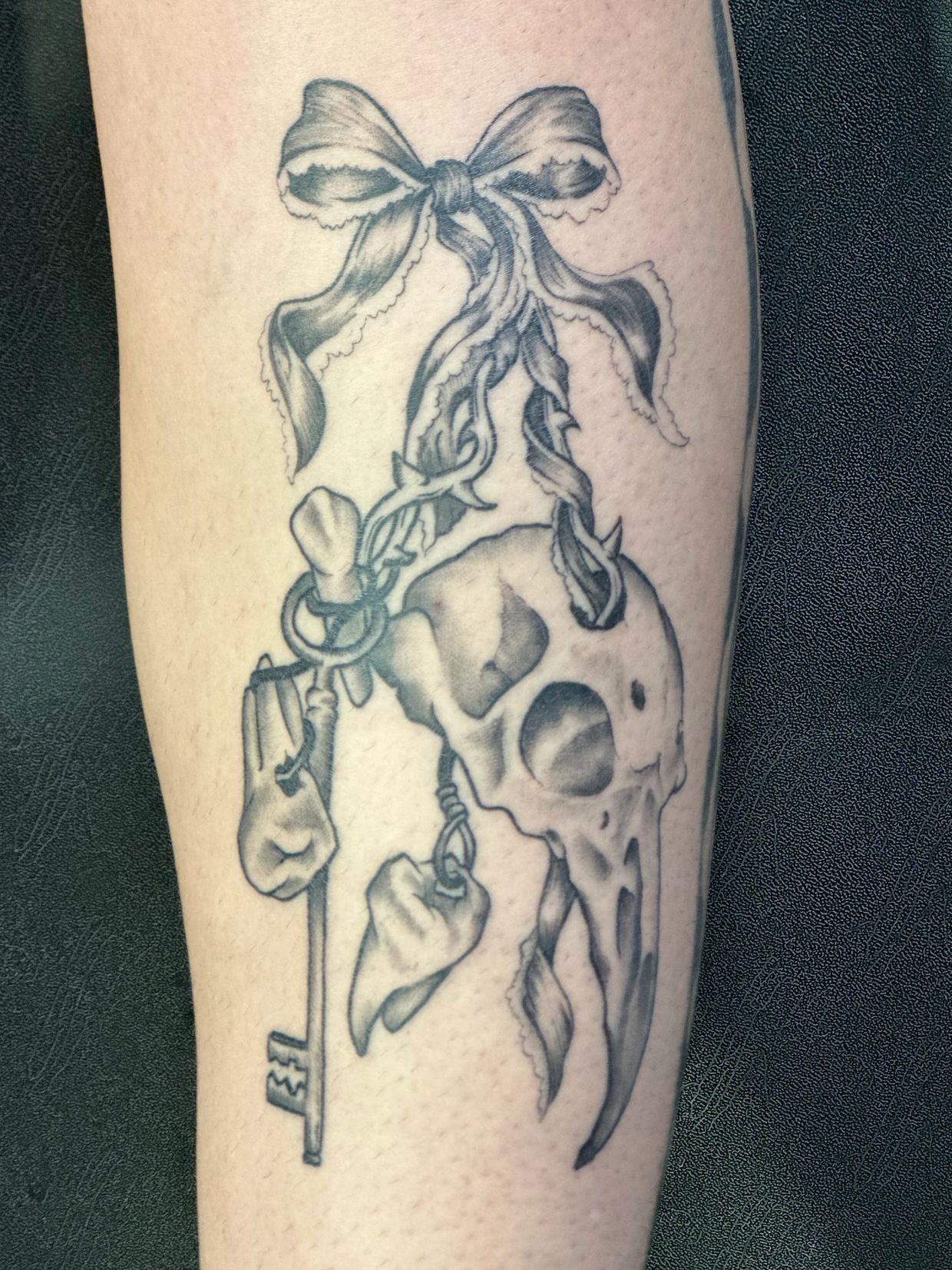 Healed black and gray illustrative tattoo featuring a skull charm, teeth, ribbon and skeleton key.