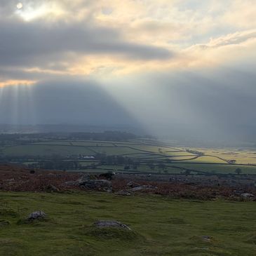 Sun rays breaking through clouds over a rocky landscape.