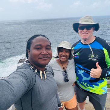 Three friends smiling at the camera with the ocean behind them.