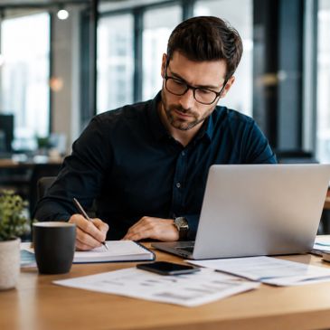 Man working on paperwork at a desk with laptop and coffee.