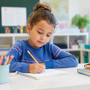 Young girl writing in a notebook at a desk.