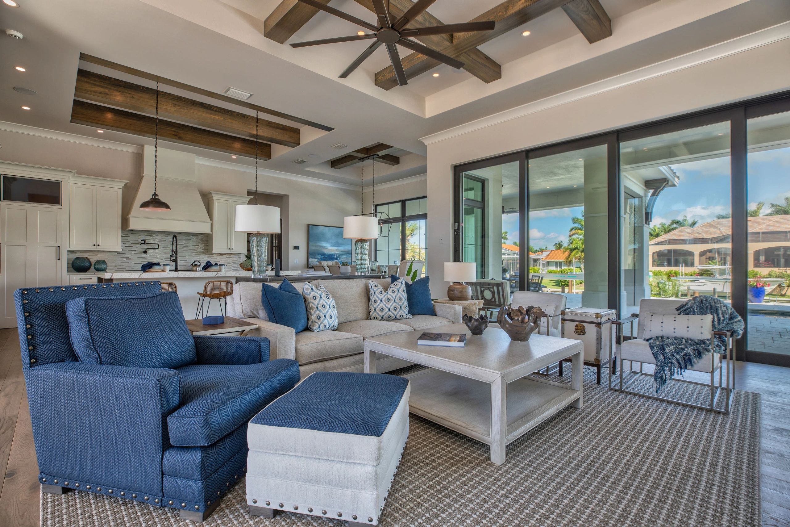 Spacious living room with blue and beige furniture, wooden beams, and large glass doors.