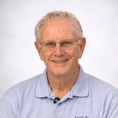 Smiling elderly man wearing glasses and a light blue polo shirt.