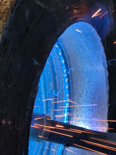 Close-up of sparks flying from metalwork inside a blue-lit machine.