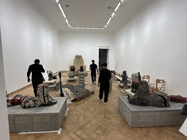 People setting up an art exhibition with stone sculptures on platforms in a gallery.
