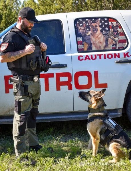 K9 officer and German Shepherd police dog beside a patrol vehicle.