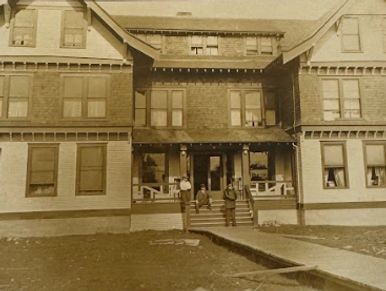 The McCleary Hotel, 1912: People sitting on porch; boardwalk; no gardens; 2 tone paint; front doors