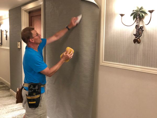 Man installing or smoothing wallpaper in a hallway.