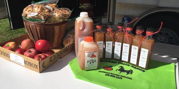 Display of fresh apples, apple cider, and apple chips at a market stall.