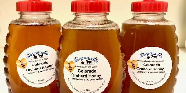Three bottles of Colorado Orchard Honey with red caps.
