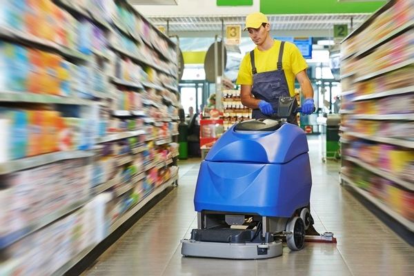 commercial cleaner using auto scrubber machine to clean grocery store floors wearing yellow t shirt 