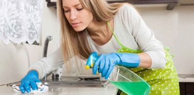 blonde lady spraying sanitizer on kitchen counter wearing gloves and white shirt