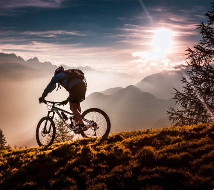 Mountain biker rides at sunset on a ridge with scenic mountains.