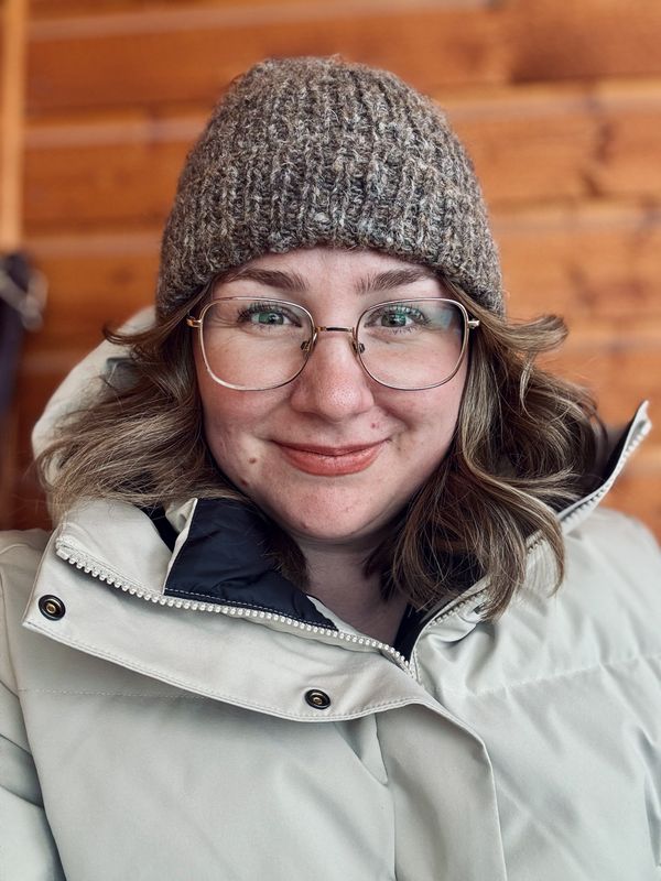 A smiling woman wearing glasses, a knitted hat, and a winter coat.