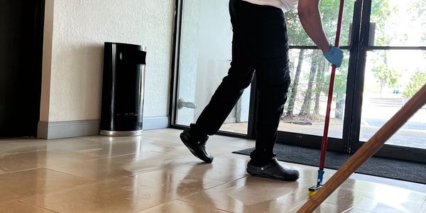 Person mopping the floor near glass doors in a well-lit room.