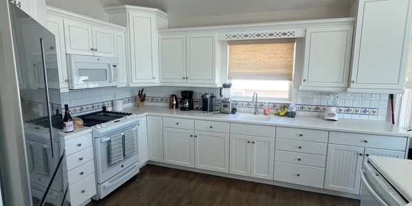 Bright white kitchen with modern appliances and wooden floor.