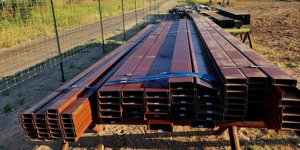 Steel building materials on pallets next to a chain link fence.