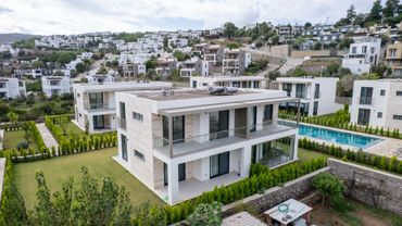 Modern white villas with glass balconies and a swimming pool in a hillside community.