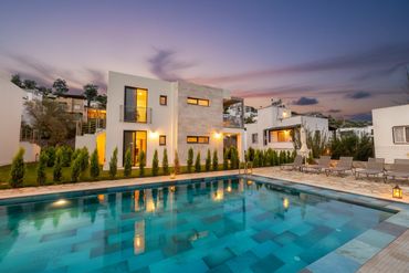 Modern house with illuminated windows and a swimming pool at dusk.