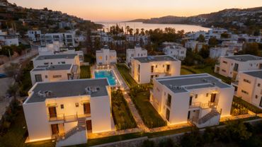 Modern white villas with a pool at sunset overlooking a coastal area.