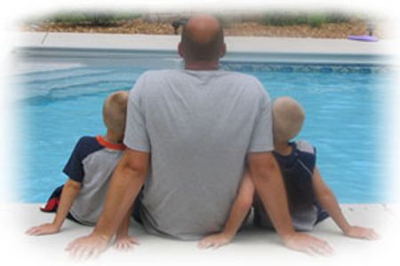 A man sitting by the pool between two young boys