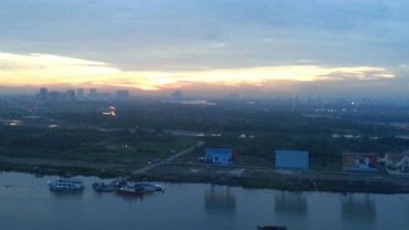 Sunset over a river with boats and distant city skyline.
