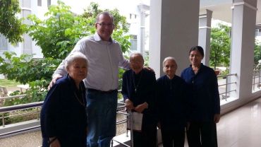 A man posing with four elderly women outdoors near a building.