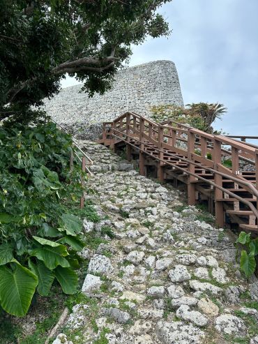 Old stone wall and pathway with greenery and wooden stairs.