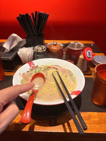A bowl of ramen with chopsticks and a red spoon in a Japanese restaurant.