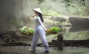 Woman in traditional Vietnamese attire carrying baskets with vegetables.