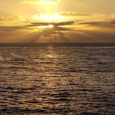Golden sunset over the ocean with sun rays through clouds.