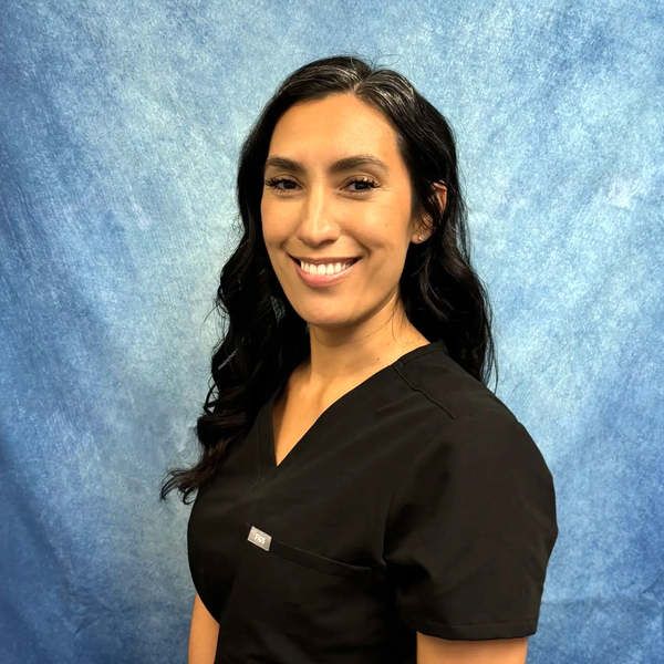Smiling woman in black medical scrubs in front of blue backdrop.