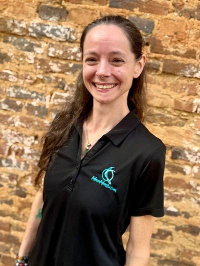 Smiling woman in a black polo shirt stands against a rustic brick wall.