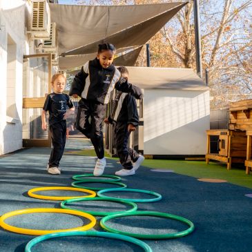 Children playing hopscotch with colored hoops outdoors.