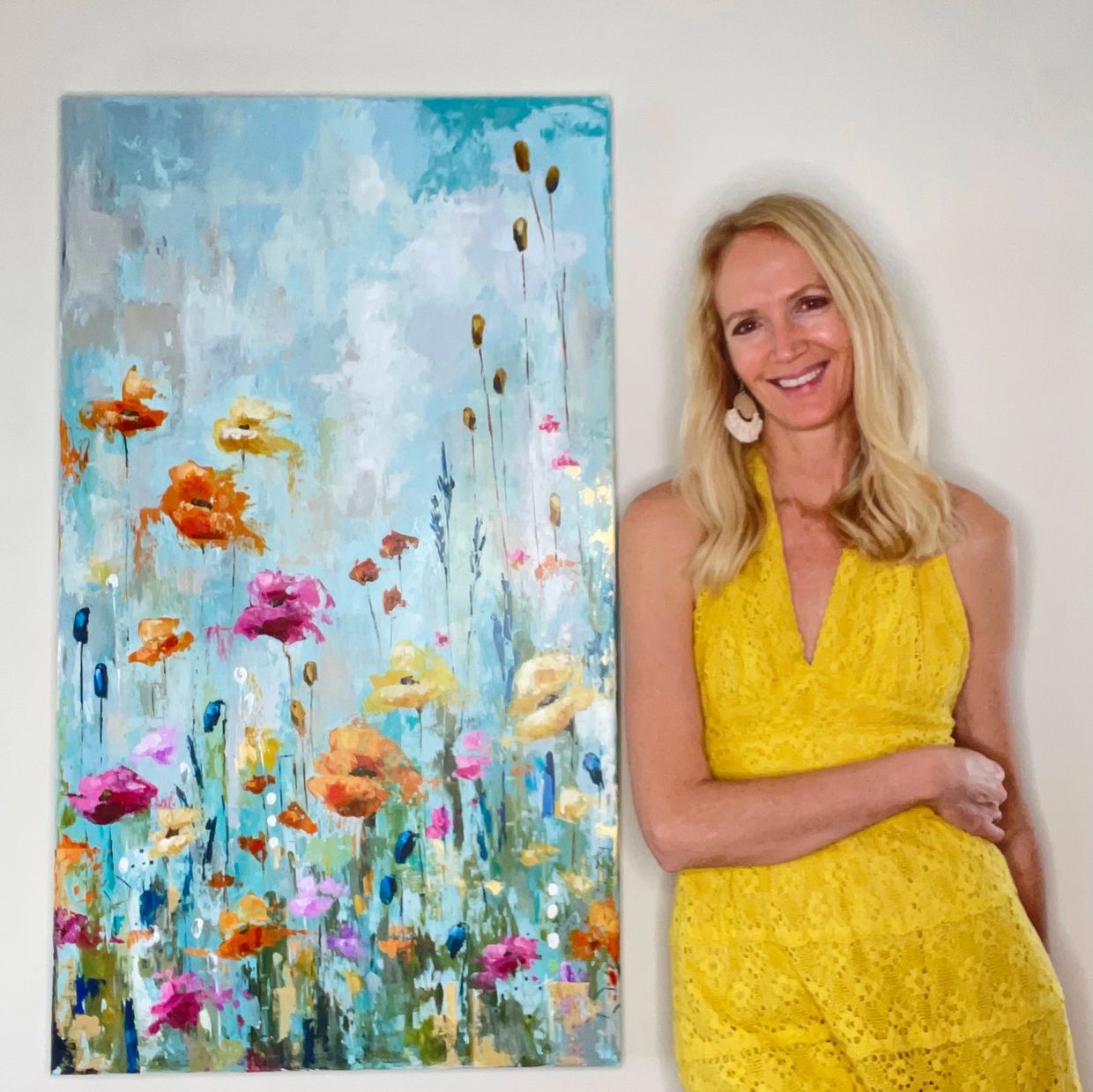 Woman in yellow dress beside colorful flower painting.