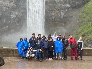 Group of teenagers in rain gear posing by a waterfall on a rainy day.