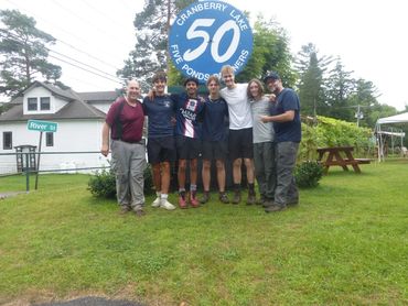 Group of seven men posing happily in front of a Cranberry Lake sign.