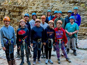 A group of kids wearing helmets and harnesses for rock climbing.