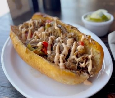 A Philly cheesesteak sandwich drizzled with sauce on a white plate.