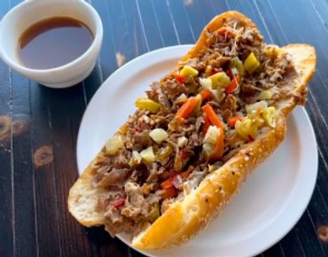 Open sandwich with pulled meat and vegetables beside a cup of sauce.