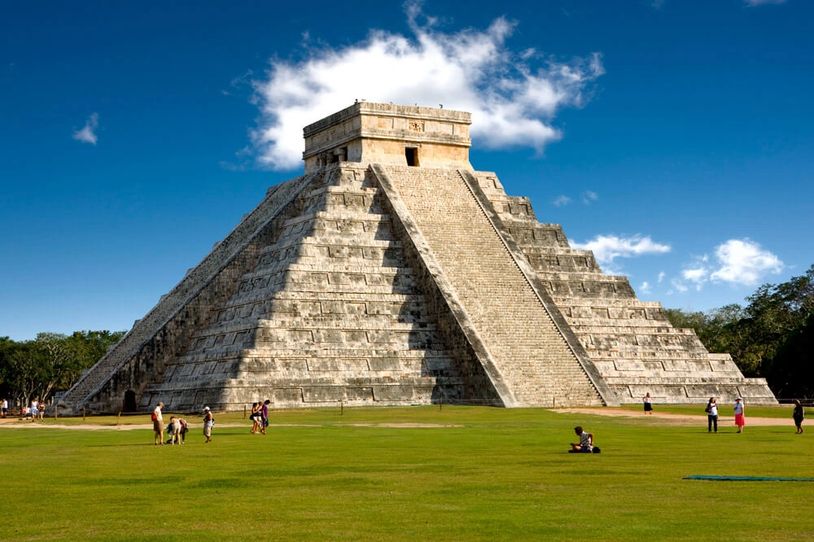 The ancient Mayan pyramid of Chichen Itza under a blue sky.