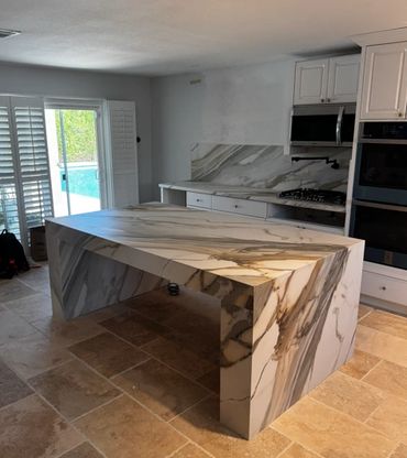 Modern kitchen with a large marble island and natural stone floor.