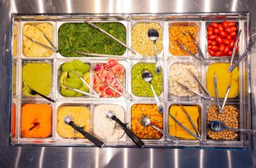 Fresh salad bar with various vegetables and toppings in a stainless steel tray.