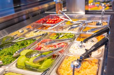 Colorful salad bar with fresh vegetables and tongs.