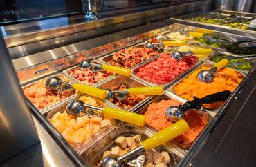 A salad bar with various diced vegetables and meats in trays.